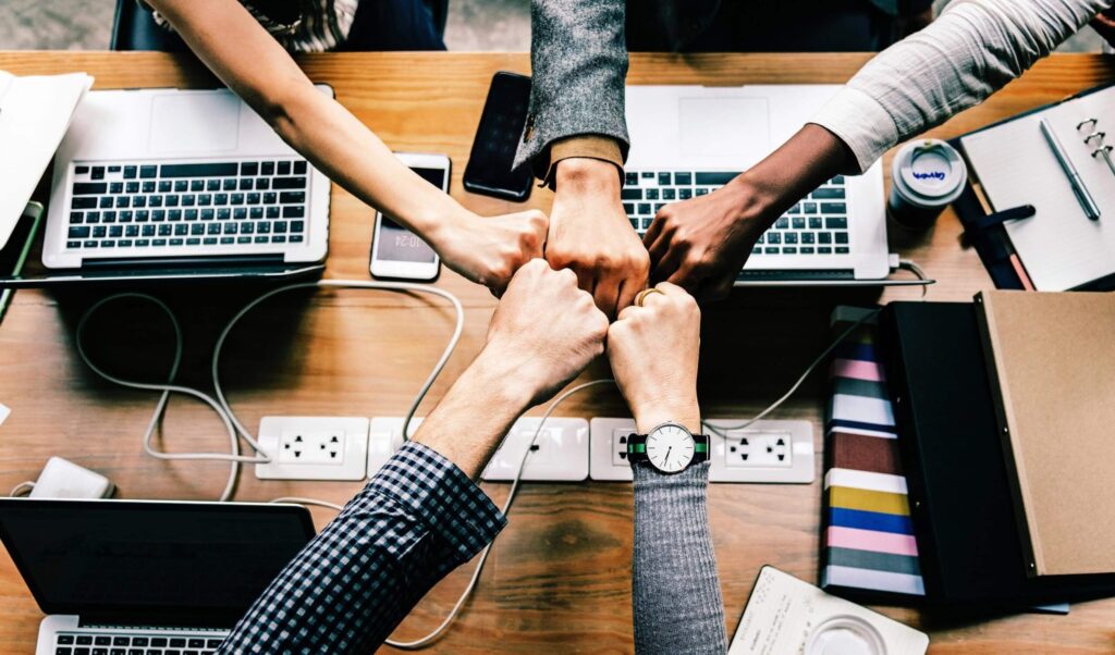 Software developers fist bumping each other over laptops and mobile devices