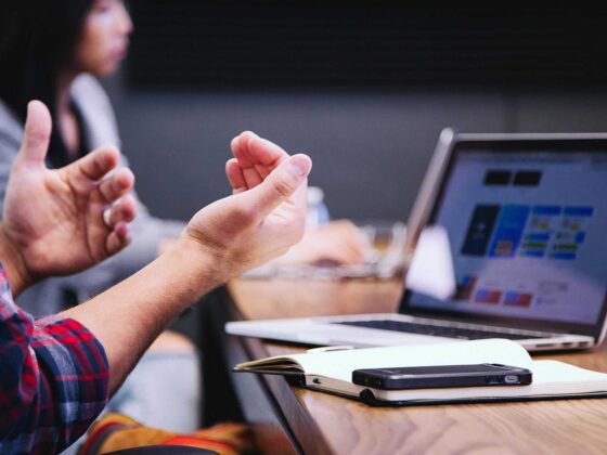 Product Owner in a meeting with hands up in front of apple laptop and iPhone 8 mobile devices