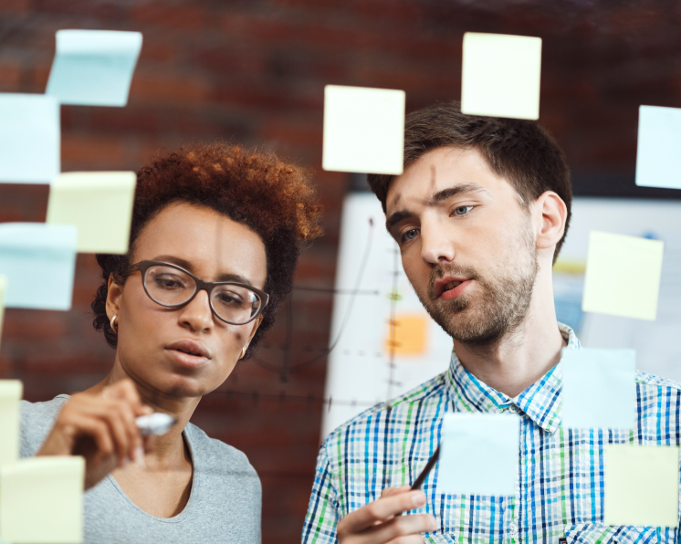 male and female coworkers work together to solve a problem using a dry-erase board