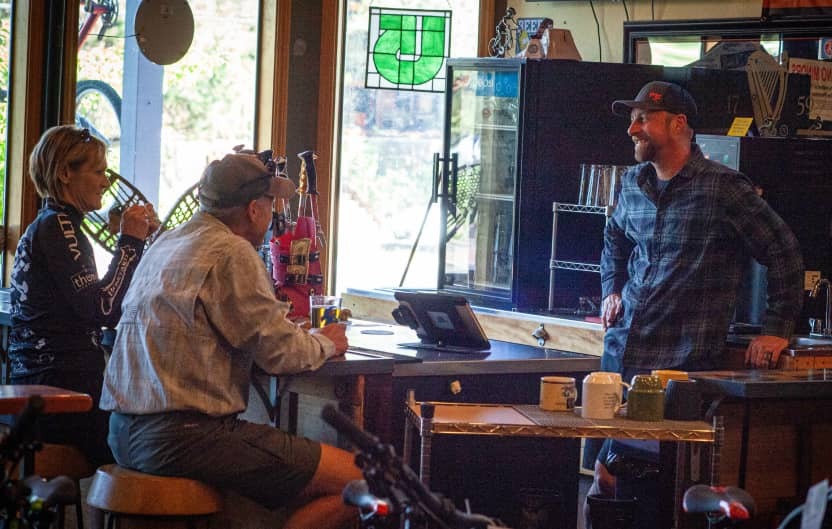 A photograph of the Sagebrush Cycles bar. A local drinks and chats with the bartender.
